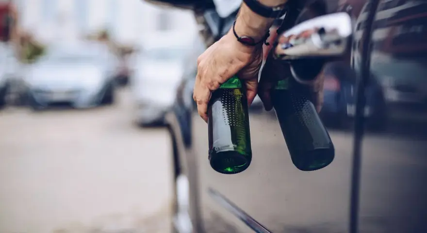 Mann hält zwei Bierflaschen aus dem Autofenster. Er versucht, den Alkohol abzubauen, indem er sie wegwirft.