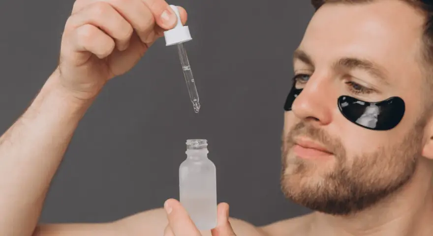 Homme avec patchs oculaires noirs appliquant un sérum. Découvrez les acide glycolique bienfaits pour une peau éclatante.