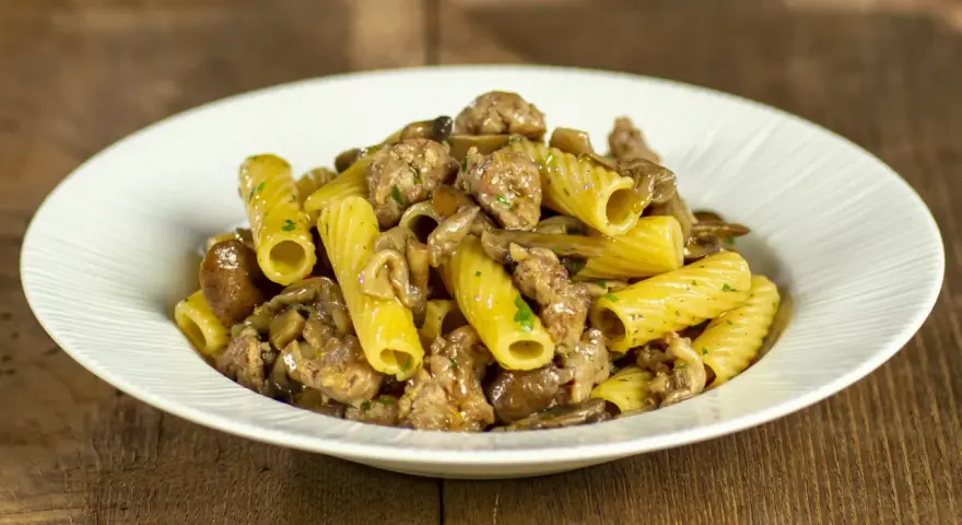 Piatto di pasta funghi e salsiccia, con rigatoni conditi con funghi trifolati e pezzetti di salsiccia saporita.