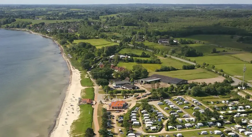 Luftaufnahme eines Campingplatzes in Schleswig-Holstein mit Wohnmobilen und Zelten, direkt am sandigen Strand und dem Meer gelegen.