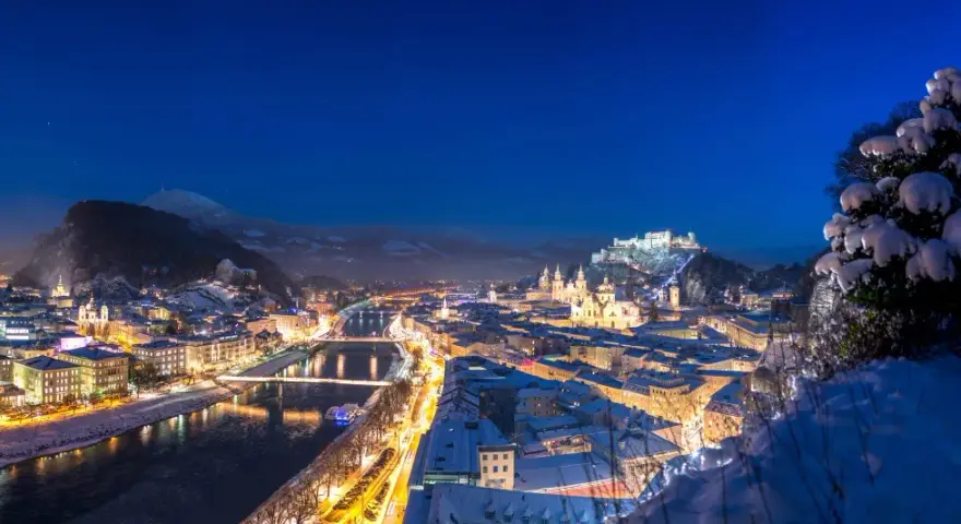 Magiczne salzburg zimą. Oświetlone miasto, rzeka Salzach i górująca twierdza Hohensalzburg w śnieżnej scenerii nocą.