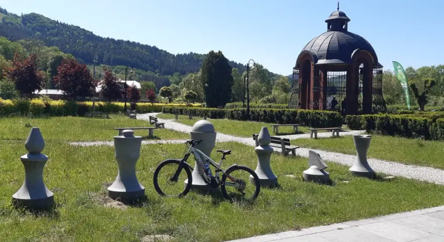 Rower czeka na ścieżce w Piwnicznej-Zdroju, wśród kamiennych figur i zieleni.