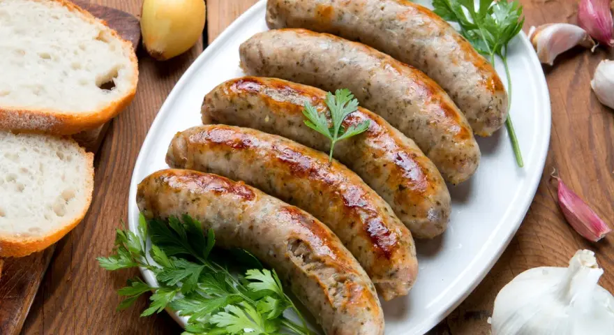 Pięć soczystych białych kiełbasek z piekarnika, podanych z chlebem, cebulą i czosnkiem.