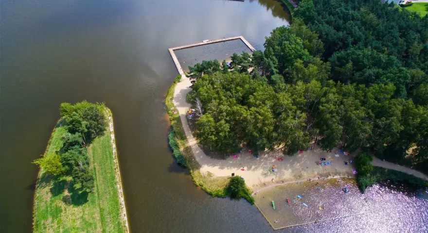 Widok z lotu ptaka na jezioro z kąpieliskiem, plażą i lasem.