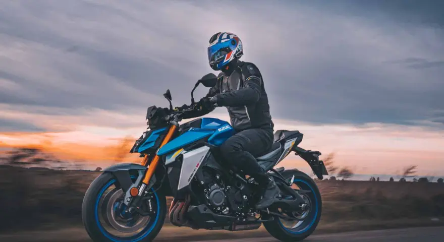 Motocyklista w kasku jedzie na niebieskim Suzuki GSX-S1000 podczas zachodu słońca.