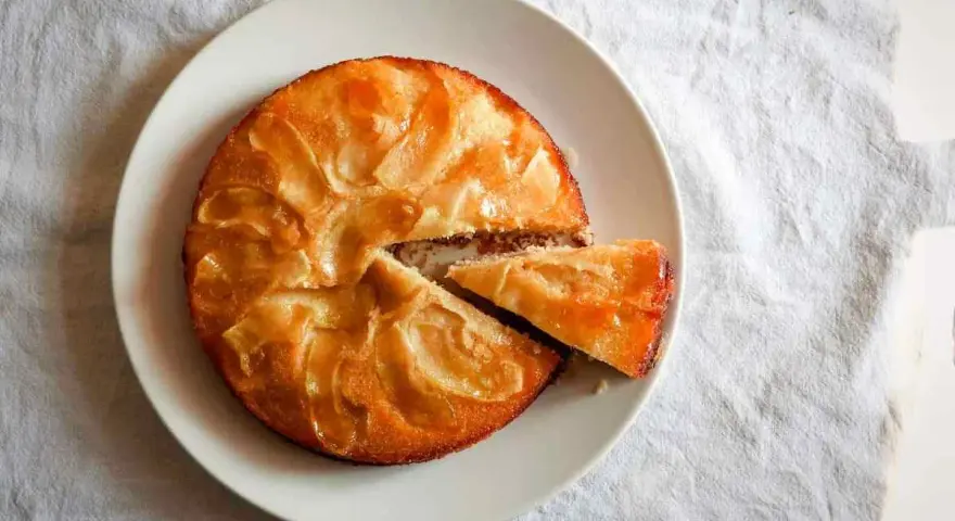 Tarta de manzana esponjosa, dorada y jugosa, con una porción recién cortada lista para disfrutar.