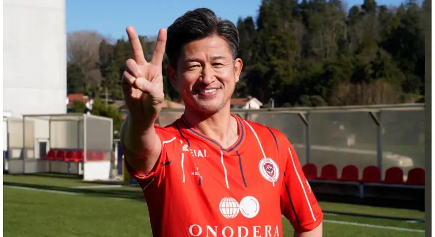 Uśmiechnięty Kazuyoshi Miura, najstarszy piłkarz na świecie, pokazuje znak pokoju na boisku.