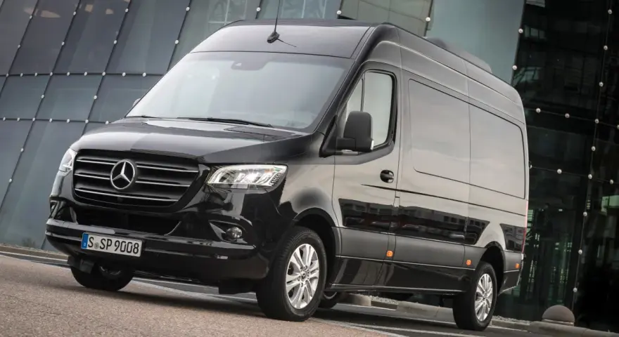 Czarny furgon Mercedes-Benz Sprinter stoi przed nowoczesnym budynkiem z przeszkloną fasadą.