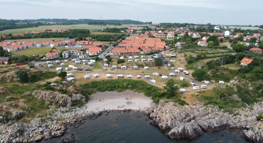 Sannes familjecamping vid kusten, med husvagnar och tält utspridda bland klippor och grönska.