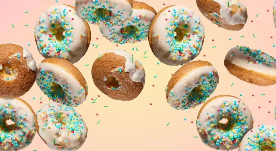 Bunte Donuts mit weißer Glasur und Streuseln schweben im Bild. Ein köstliches Rezept für selbstgemachte Donuts.