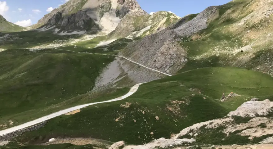 Strada bianca serpeggia tra verdi colline e rocce, verso un monte imponente. Un'avventura in **moto** su una **colle fauniera** panoramica.