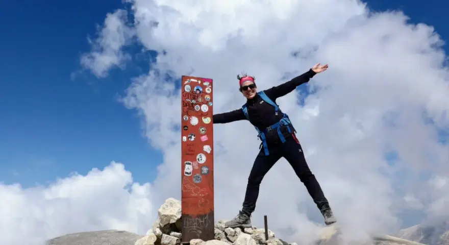 Donna esulta in cima al Monte Amaro dopo un trekking. Cielo azzurro e nuvole bianche.