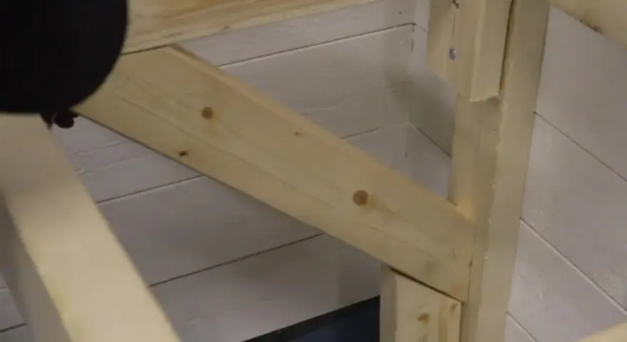 En person håller på att såga snett en träbit som ska bli en del av en konstruktion.