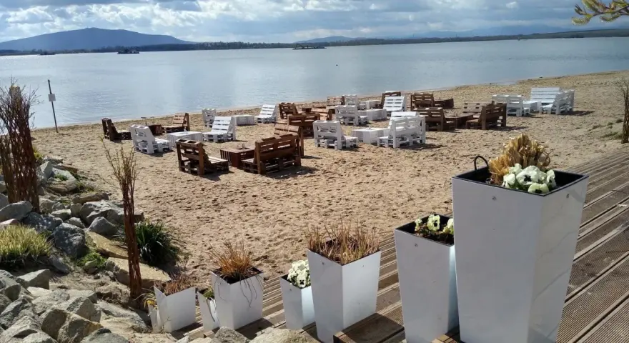 Plaża nad mietkowym zalewem z meblami z palet. W oddali góra i jezioro.