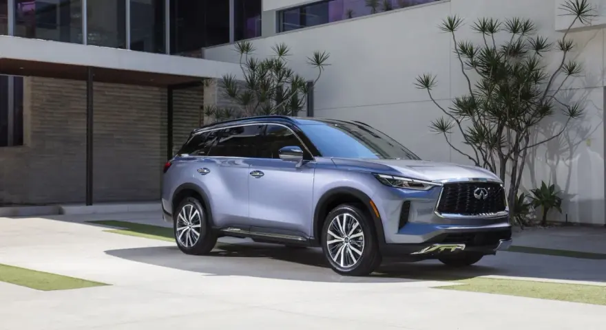 Elegancki, srebrny infiniti samochód zaparkowany przed nowoczesnym budynkiem z kamienną fasadą i dużymi oknami.