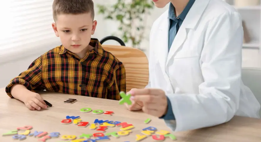 Chłopiec z dysleksją układa litery z terapeutką. Czy dysleksja to choroba? Terapia pomaga w nauce.