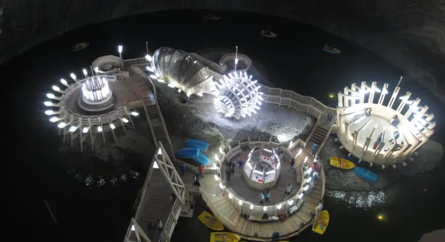 Podziemne jezioro w **Salina Turda** z łódkami i oświetlonymi platformami.