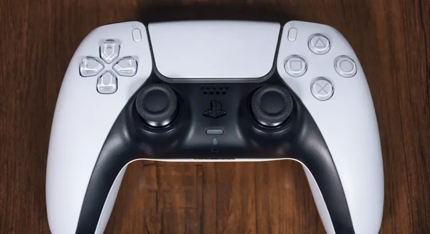 Biały kontroler DualSense do PS5 leży na drewnianym blacie. Zastanawiasz się nad ps4 pobór prądu?
