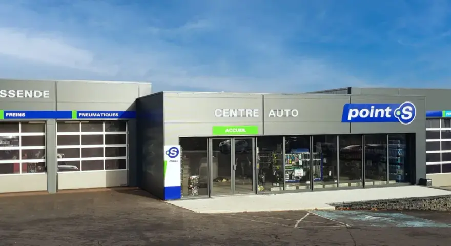 Façade d'un centre auto Point S avec des portes de garage et des panneaux indiquant les services (vidange, freins, pneumatiques, pare-brise).