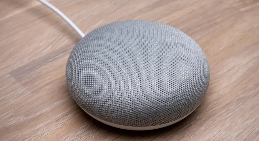 En grå Google Home Mini på ett trägolv, redo att styra ditt smarta hem med Verisure.