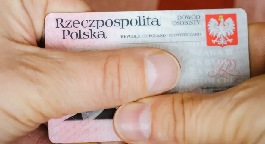 Dłonie trzymają polski dowód osobisty. Widoczny jest numer dowodu osobistego.