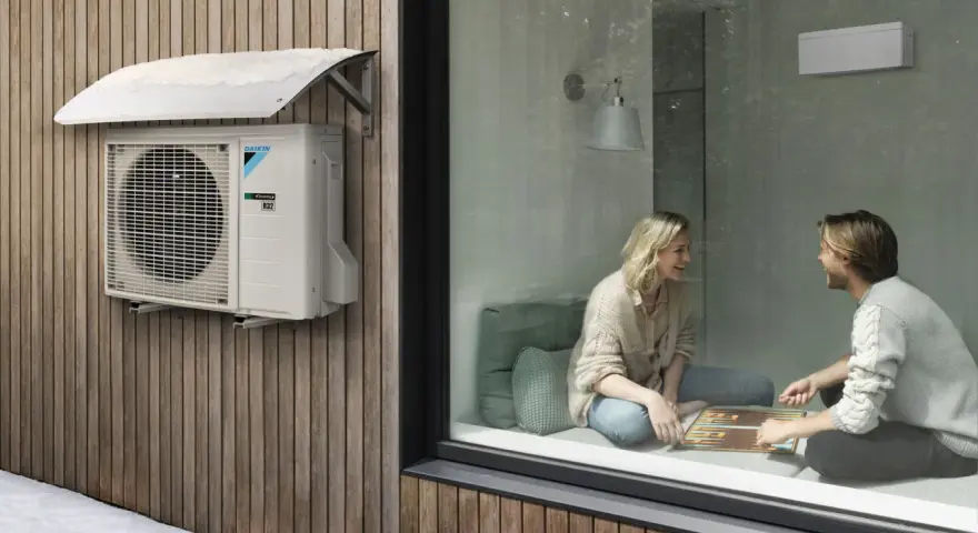 Unidad exterior de aire acondicionado Daikin instalada bajo un alero protector en una pared de madera. Ideal para saber donde colocar la unidad exterior del aire acondicionado.