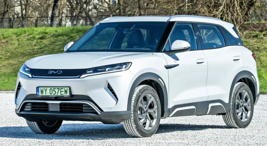 Biały SUV z logo BYD, jeden z chińskich samochodów elektrycznych, zaparkowany na żwirowej nawierzchni.