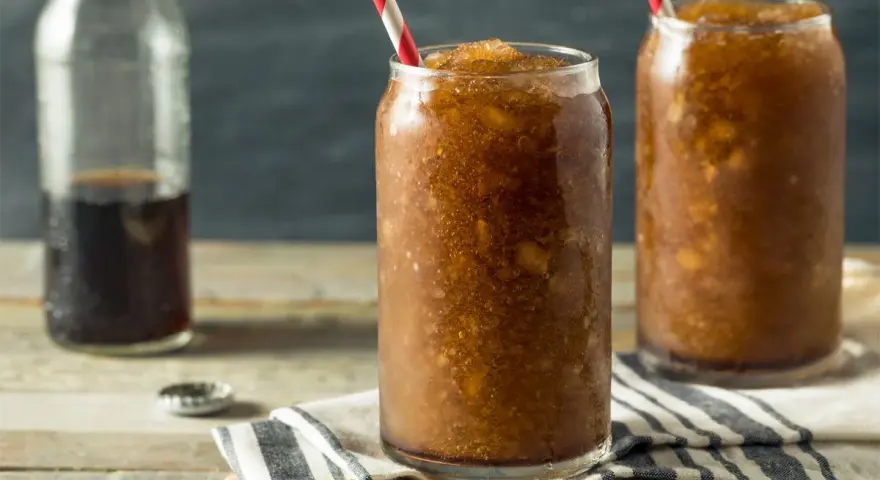 Zwei Gläser mit erfrischendem Cola Slush Eis, bereit zum Genießen. Eine Flasche Cola steht daneben.