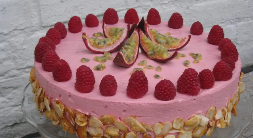 En rosa hallonmousse tårta dekorerad med färska hallon och passionsfrukt. Kanterna är täckta med rostade mandelflagor.