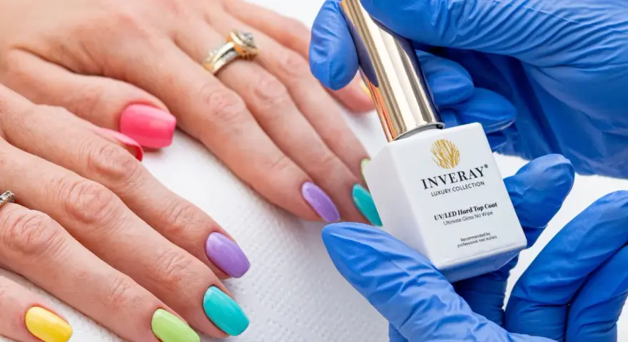 Kolorowy manicure hybrydowy krok po kroku. Dłoń z paznokciami w pastelowych barwach, kosmetyczka trzyma buteleczkę lakieru.