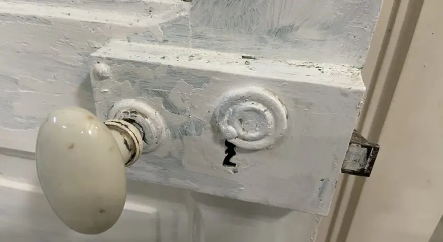 Poignée de porte ancienne recouverte de peinture blanche écaillée, prête à être nettoyée.