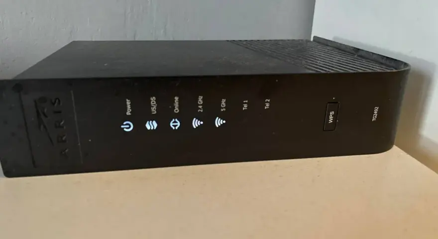 Czarny router Arris TG2492 z widocznym przyciskiem WPS i wskaźnikami stanu: Power, US/DS, Online, 2.4 GHz, 5 GHz, Tel 1, Tel 2.