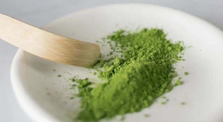 Zielony proszek matcha na białej miseczce z bambusową łopatką.