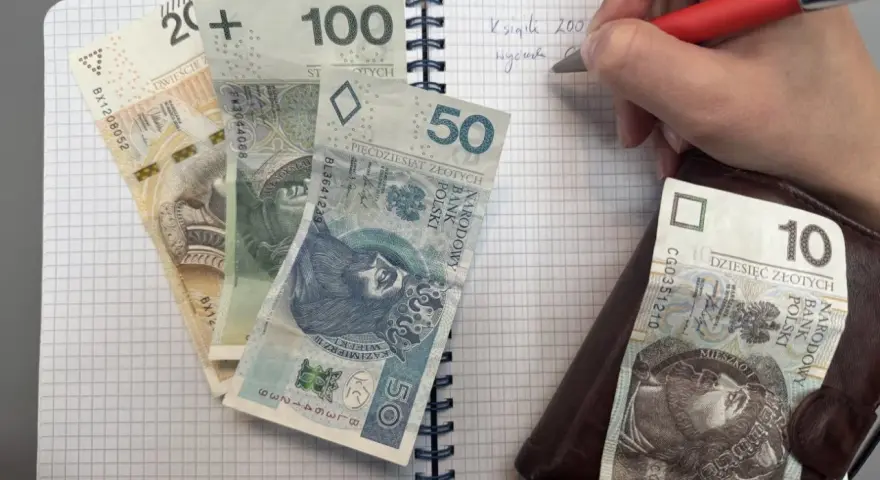 Zapisywanie wydatków na dziecko z orzeczeniem o potrzebie kształcenia specjalnego. Na zeszycie leżą banknoty 200, 100, 50 i 10 zł.