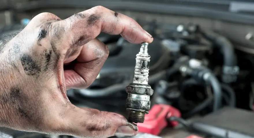 A mechanic's greasy hand holds a used spark plug, a reminder that many cars still have spark plugs for ignition.
