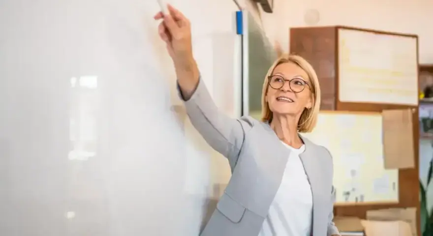 Nauczycielka z markerem przy tablicy, uśmiechnięta. To może być ocena pracy nauczyciela początkującego, który właśnie prezentuje swoje umiejętności.