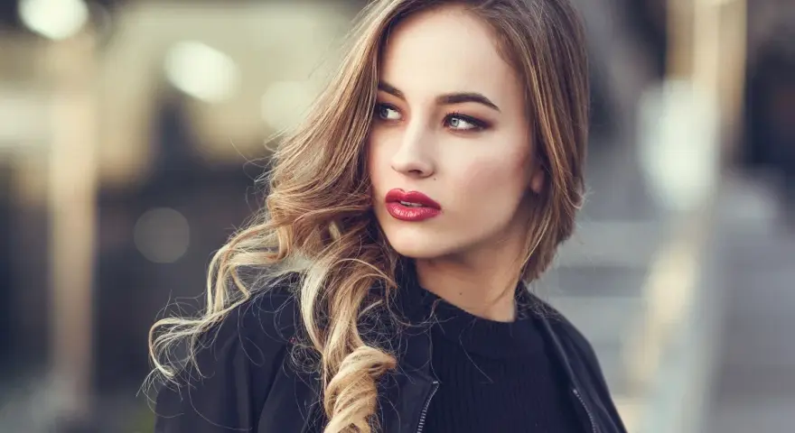 Blondynka z burzą falowanych włosów i wyrazistymi, czerwonymi ustami. Idealny kolor pomadki dla blondynek podkreśla jej urodę.