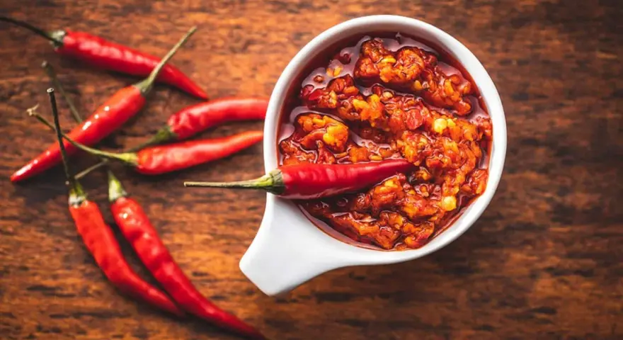 Scharfes Essen stillen: Eine Schale mit feuriger Chilisauce und frischen roten Chilis auf einem Holztisch.