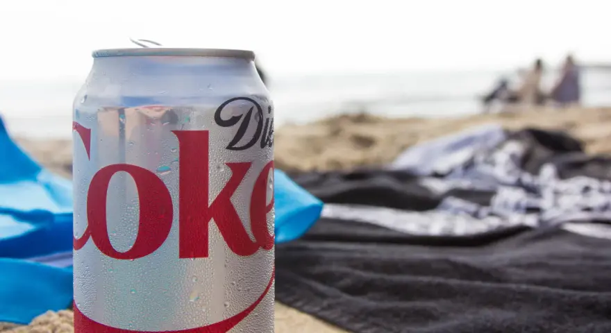 En burk Diet Coke på stranden, perfekt för den som vill undvika socker och hantera diabetes. Sukralos i drycken gör den till ett sockerfritt alternativ.