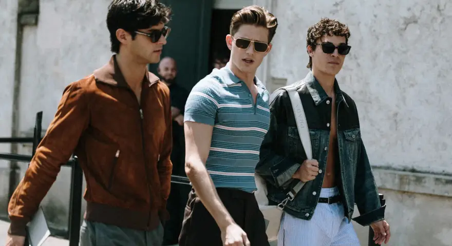 Tre uomini camminano insieme, uno con giacca marrone, uno con polo a righe e uno con giacca di jeans. Un look uomo di stile.