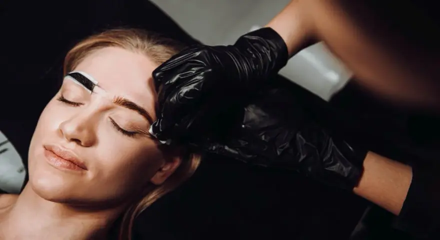 Stylistka w czarnej rękawiczce precyzyjnie maluje brwi klientce. Zastanawiasz się, co ile henna brwi daje najlepsze efekty?