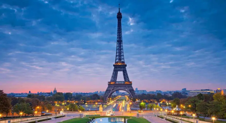 Torre Eiffel iluminada al atardecer, uno de los iconos franceses más reconocidos, con el cielo azul y nubes rosadas.