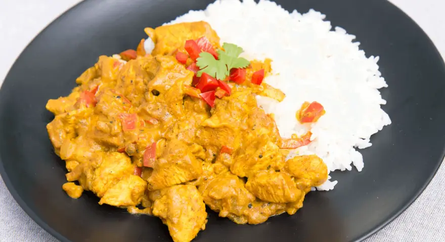 Pyszny kurczak curry fit z ryżem, papryką i kolendrą na czarnym talerzu. Idealny posiłek dla dbających o linię.