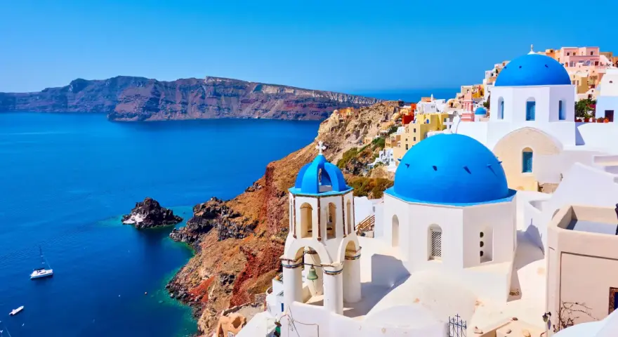Santorini wakacje: białe domy z niebieskimi kopułami na tle turkusowego morza i klifów. Idealne miejsce na wymarzone wakacje.