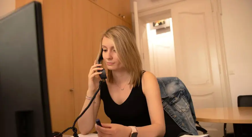 Une jeune femme blonde, en pleine journée de solidarité stagiaire, est au téléphone dans un bureau.