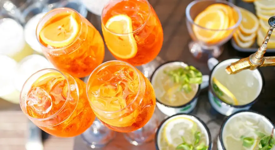Orzeźwiający drink z prosecco, udekorowany plasterkiem pomarańczy, czeka na gości. Obok inne napoje z miętą i cytryną.