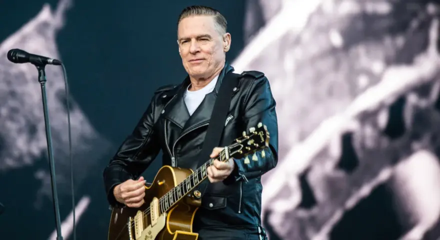 Bryan Adams w skórzanej kurtce gra na gitarze, przypominając piosenkę z Robin Hooda.