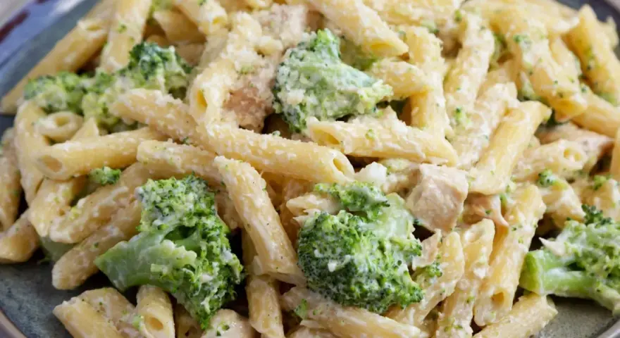 Penne z kurczakiem i kremowym sosem, obficie posypane zielonymi różyczkami brokułów. Pyszne makaron z brokułami na talerzu.