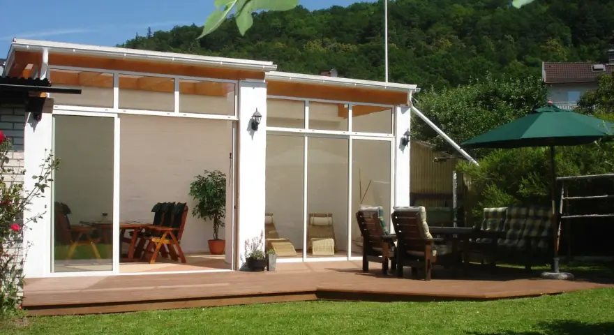 En modern glasveranda med trädgårdsmöbler och parasoll. Perfekt uteplats inspiration för soliga dagar.