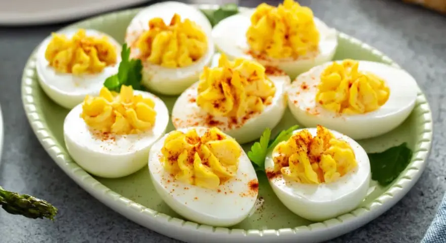 Oeufs mimosa au thon, garniture jaune crémeuse saupoudrée de paprika sur des blancs d'œufs sur une assiette verte.